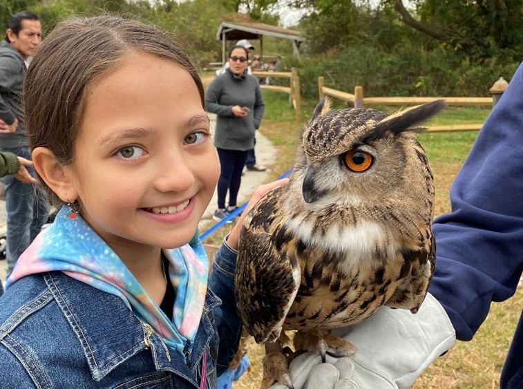 A Raptorama participant smiles as she poses next to a Great Horned Owl held by a raptor rehabilitator. Photo: Don Riepe
